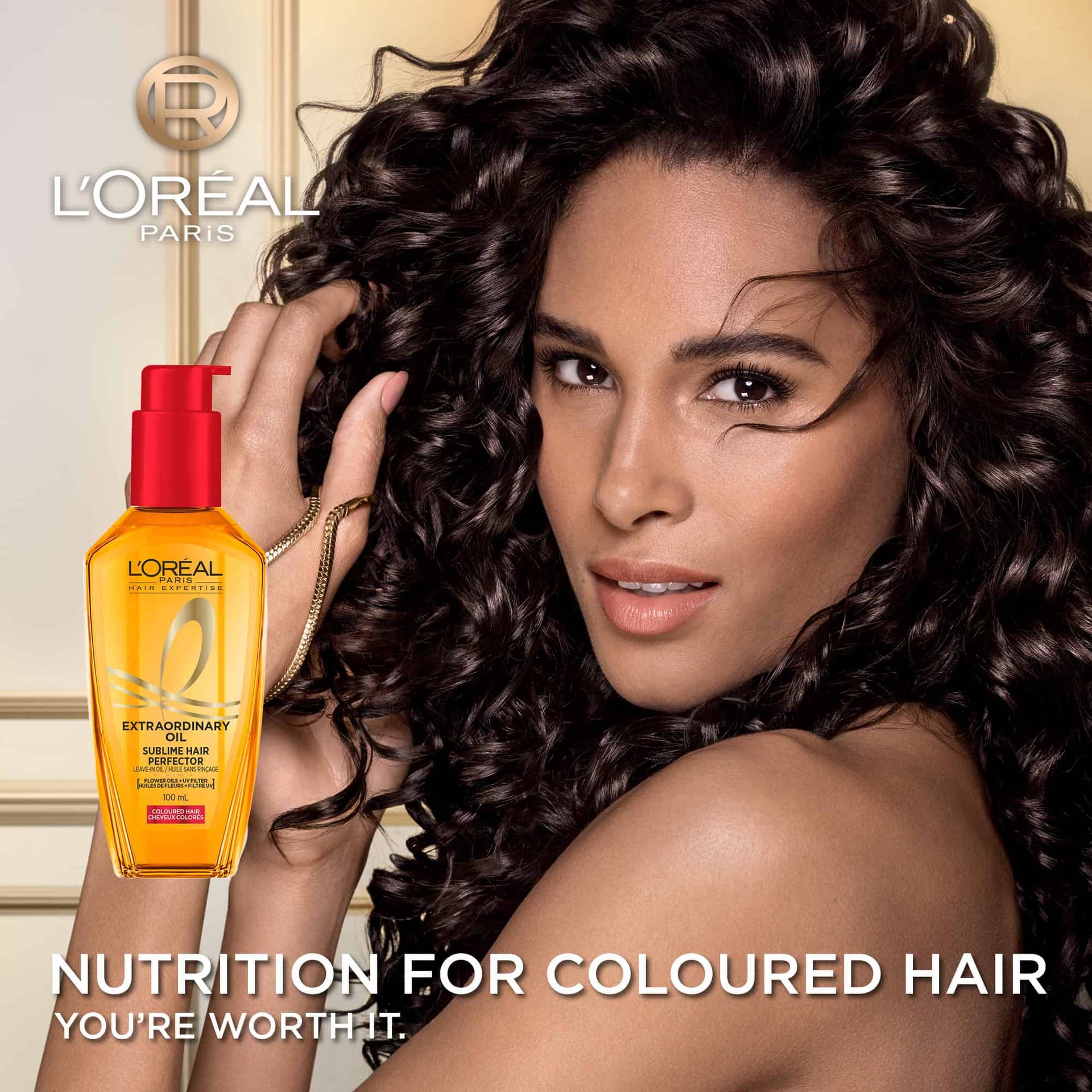 A woman with voluminous, shiny dark curly hair smiling next to a bottle of L'Oréal Paris Extraordinary Oil on a light background. Below, text reads "Nutrition for Coloured Hair".