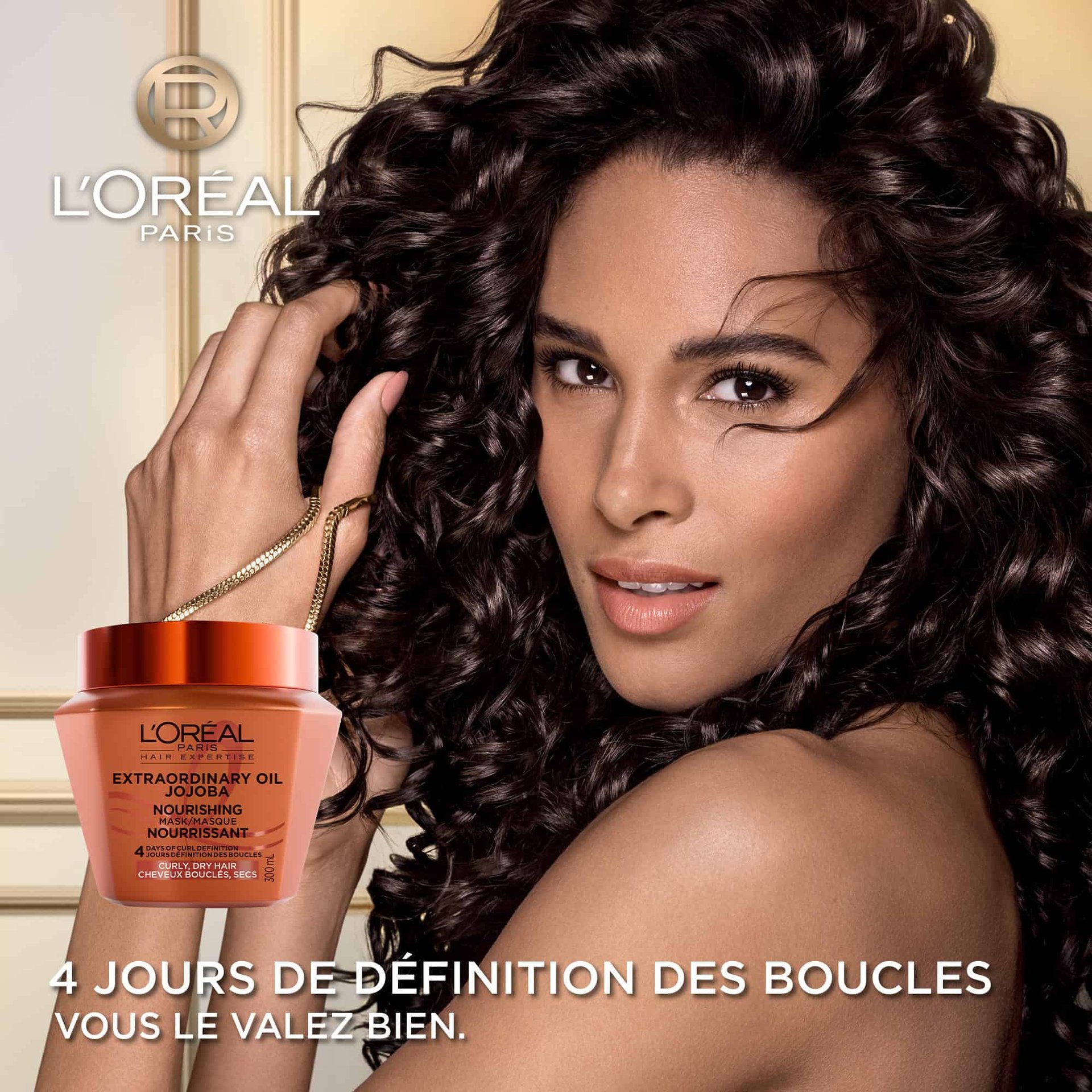 Une femme aux cheveux bouclés foncés, volumineux et brillants regardant l'objectif. En bas à gauche, le pot de masque de jojoba s'affiche avec le texte « Boucles définies pendant 4 jours ».