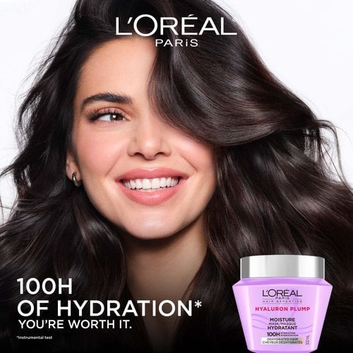 A close-up view of a smiling woman with voluminous, shiny, and wavy dark hair. To her left, the text reads "100H of hydration", with the purple hair mask jar in the bottom corner.