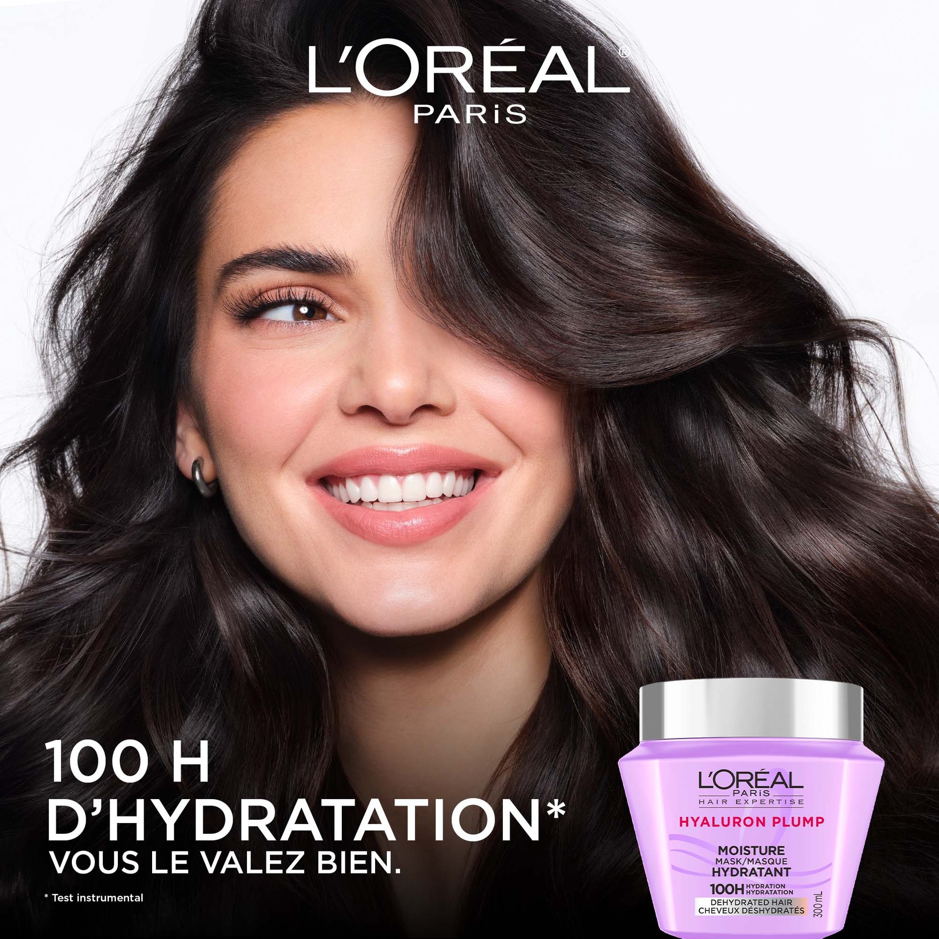 Gros plan d'une femme souriante aux cheveux longs noirs, volumineux, souples et brillants. À sa gauche, le texte indique « 100 h d'hydratation » avec le pot de masque violet en bas.
