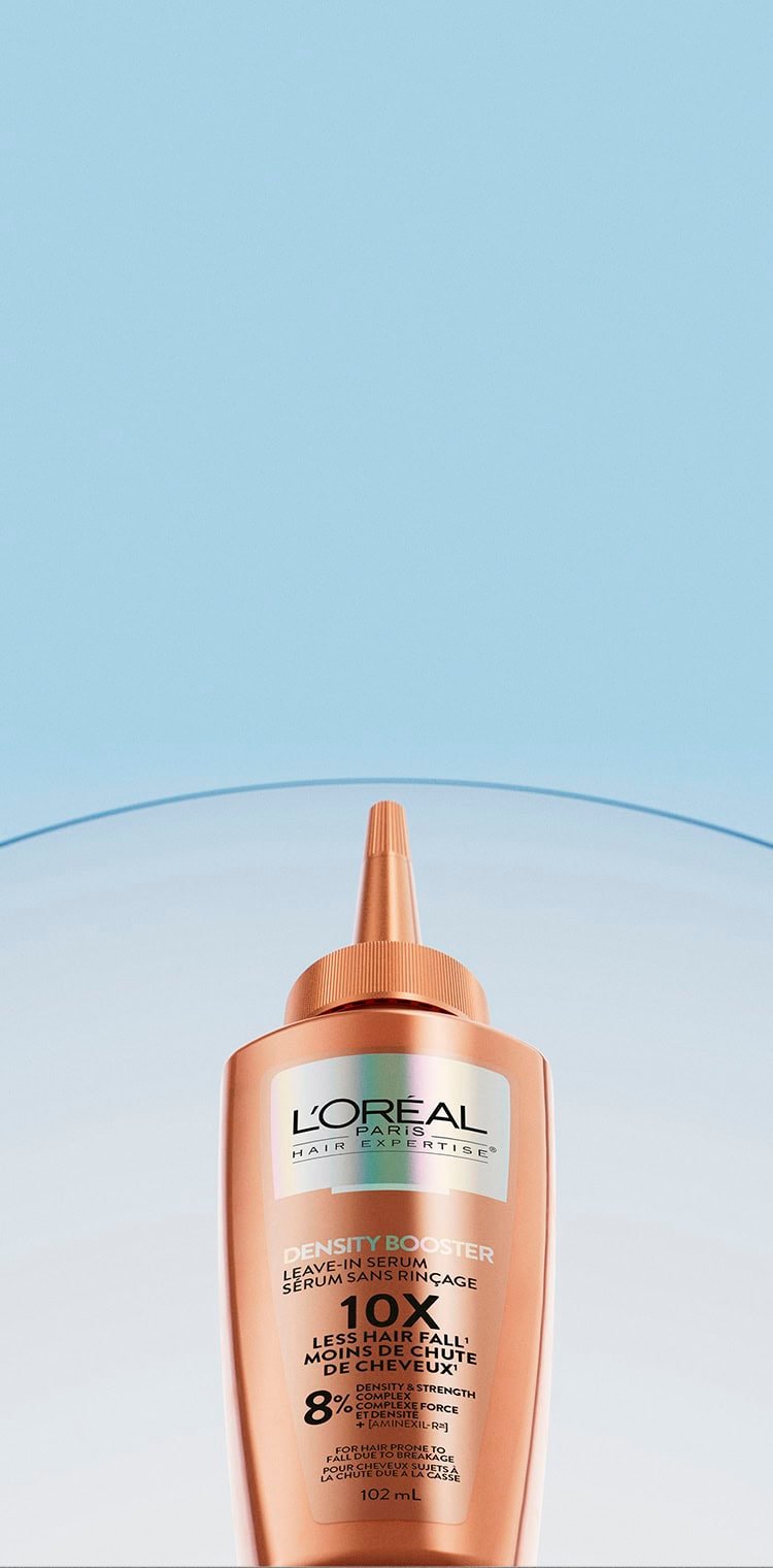 Flacon de sérum sans rinçage L'Oréal Paris Hair Expertise Density Booster, de couleur cuivrée, avec un embout applicateur fin. Le flacon affiche les mentions "Leave-In Serum/Sérum Sans Rinçage", "10x Less Hair Fall/Moins de Chute de Cheveux", "8% Density & Strength Complex" et "For Hair Prone to Fall/Cheveux Sujets à la Chute". Il est présenté sur un fond bleu dégradé avec une bande translucide courbée