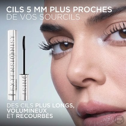 Gros plan sur l'œil d'une mannequin avec des cils longs et recourbés. À gauche, un tube argenté de mascara L'Oréal "Telescopic Extensionist" avec sa brosse. Le texte en haut indique "CILS 5 MM PLUS PROCHES DE VOS SOURCILS" et en bas "DES CILS PLUS LONGS, VOLUMINEUX ET RECOURBÉS".
