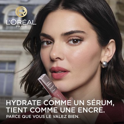 Kendall Jenner, ambassadrice L'Oréal Paris, tient le produit L'Oréal Paris Hyaluron Tint devant ses lèvres. Le texte promotionnel indique : 'HYDRATE COMME UN SÉRUM, DURE COMME UNE TEINTURE. VOUS LE VALEZ BIEN.