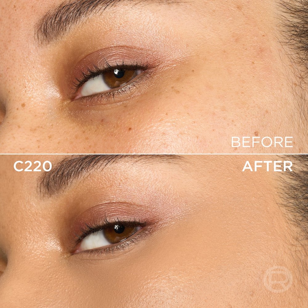 A split image showing a before and after comparison of a person's under-eye and cheek area. The top section, labeled 'BEFORE', displays skin with visible freckles, slight under-eye discoloration, and light eye makeup. The bottom section, labeled 'C220' and 'AFTER', shows the same facial area with noticeably more even-toned, smoother skin, and reduced freckles, following the application of a cosmetic product. The eye makeup remains visible. A subtle 'R' logo is also visible in the bottom right of the 'AFTER' portion