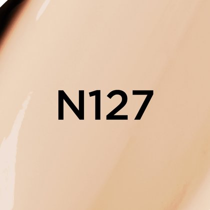 Un gros plan d'un fond de teint ou d'une texture crémeuse de couleur beige très clair avec des sous-tons neutres, avec le texte noir en gras 'N127' centré sur l'image, indiquant probablement une teinte de produit