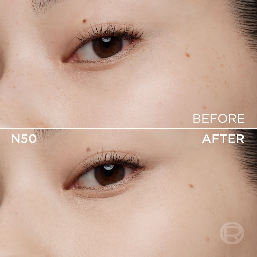 A split image showing a before and after comparison of a light-skinned person's under-eye and cheek area. The top section, labeled 'BEFORE', displays skin with a few small freckles and slight under-eye discoloration. The bottom section, labeled 'N50' and 'AFTER', shows the same facial area with noticeably more even-toned, smoother skin, and reduced imperfections, following the application of a cosmetic product. A subtle 'R' logo is also visible in the bottom right of the 'AFTER' portion