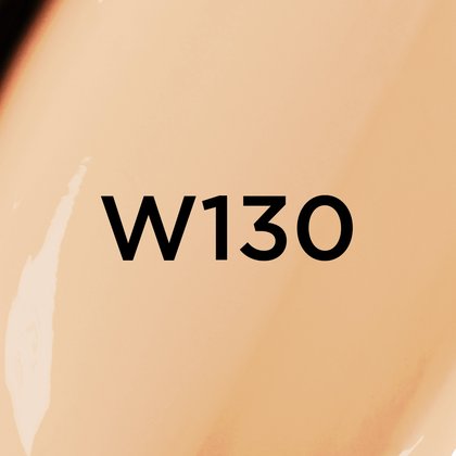 Un gros plan d'un fond de teint ou d'une texture crémeuse de couleur beige clair avec des sous-tons chauds, avec le texte noir en gras 'W130' centré sur l'image, indiquant probablement une teinte de produit