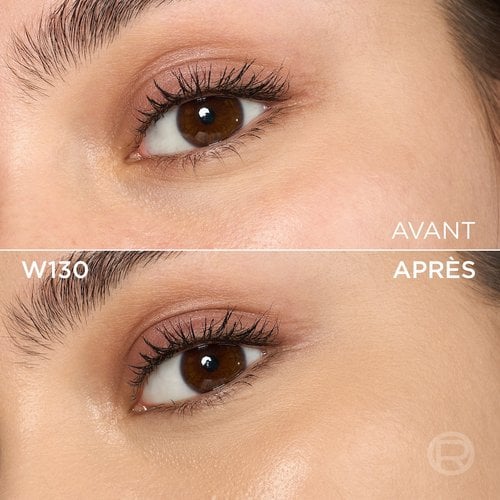 Image divisée montrant un comparatif avant et après de la zone sous l'œil et de la joue d'une personne à la peau claire à moyenne et aux yeux marron. La section supérieure, étiquetée 'BEFORE' (Avant), présente une peau avec quelques légères imperfections et une subtile décoloration sous l'œil, ainsi qu'un maquillage léger des yeux avec un fard à paupières rose-brun. La section inférieure, étiquetée 'W130' et 'AFTER' (Après), montre la même zone du visage avec une peau visiblement plus unifiée, plus lisse et des imperfections atténuées, suite à l'application d'un produit cosmétique. Le maquillage des yeux reste visible. Un discret logo 'R' est également visible en bas à droite de la partie 'APRÈS