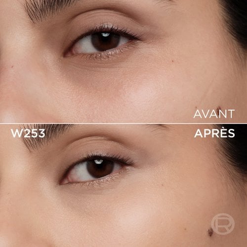 Image divisée montrant un comparatif avant et après de la zone sous l'œil et de la joue d'une personne à la peau claire à moyenne. La section supérieure, étiquetée 'BEFORE' (Avant), présente une peau avec quelques légères imperfections, une décoloration subtile sous l'œil et un maquillage discret des yeux. La section inférieure, étiquetée 'W253' et 'AFTER' (Après), montre la même zone du visage avec une peau visiblement plus unifiée, plus lisse et des imperfections atténuées, suite à l'application d'un produit cosmétique. Le maquillage des yeux reste discret. Un discret logo 'R' est également visible en bas à droite de la partie 'APRÈS