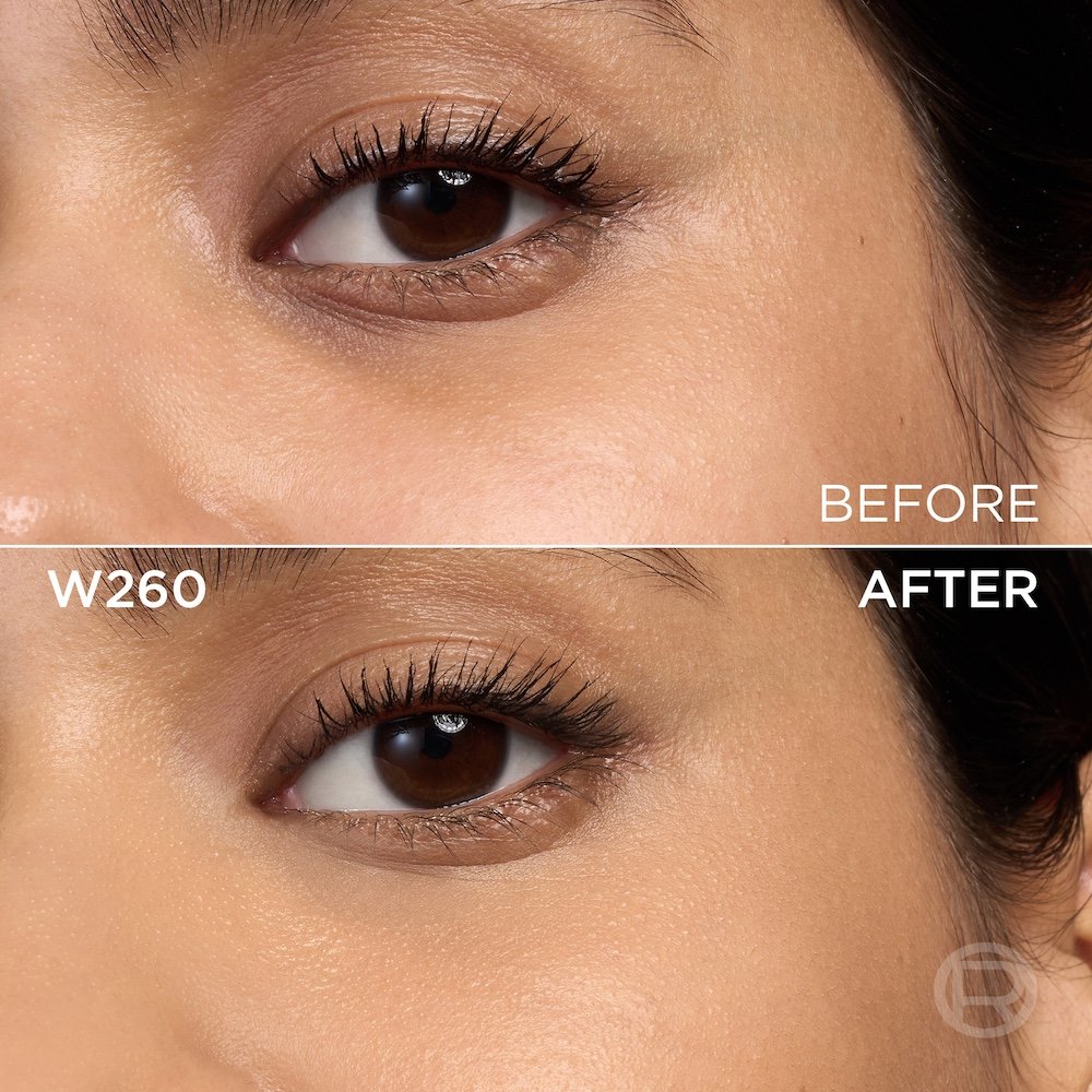 A split image showing a before and after comparison of a medium-skinned person's under-eye and cheek area with brown eyes. The top section, labeled 'BEFORE', displays skin with visible texture, pores, and slight under-eye discoloration, along with mascara applied to the lashes. The bottom section, labeled 'W260' and 'AFTER', shows the same facial area with noticeably more even-toned, smoother skin, and reduced imperfections, following the application of a cosmetic product. The mascara remains visible. A subtle 'R' logo is also visible in the bottom right of the 'AFTER' portion.