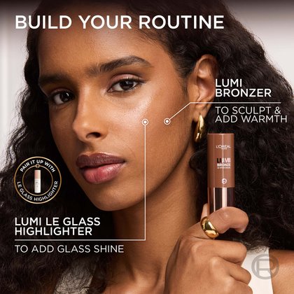 A woman with dark curly hair and a warm, medium-deep skin tone demonstrating a makeup routine. Lines on her face indicate the application areas for 'LUMI BRONZER TO SCULPT & ADD WARMTH' on her cheek and forehead, while a 'LUMI LE GLASS HIGHLIGHTER' is suggested for 'ADD GLASS SHINE' on her cheekbones. She holds a L'Oréal Lumi Bronze stick