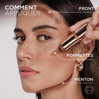 Gros plan sur le visage d'une femme au teint clair à moyen, démontrant comment appliquer le stick Lumi Bronze. Des lignes sur son front, ses pommettes et sa mâchoire indiquent les zones d'application, avec les étiquettes 'FRONT', 'POMMETTES' et 'MÂCHOIRE' à côté de chaque zone. Une main tient le stick Lumi Bronze, l'appliquant sur sa pommette
