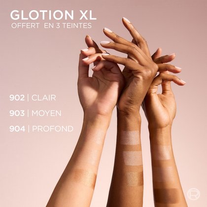 Trois mains aux tons de peau variés (clair, moyen et foncé) sont superposées, s'étendant du bas droit vers le centre, sur un fond rose pâle. Chaque main présente un échantillon d'un produit chatoyant sur l'avant-bras, correspondant à trois teintes : "902 | LIGHT" (sur la peau la plus claire), "903 | MEDIUM" (sur la peau moyenne), et "904 | DEEP" (sur la peau la plus foncée). Le haut de l'image affiche le texte "GLOTION XL DISPONIBLE EN 3 TEINTES".