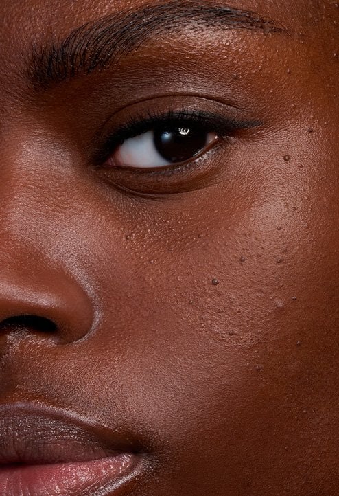 Extreme close-up "After" shot of a model's radiant deep skin, demonstrating the foundation's ability to provide luminous coverage while maintaining skin texture.