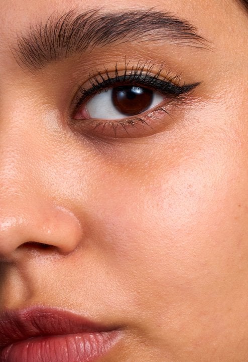 Close-up "Before" shot of a model with a tan skin tone, showing natural skin texture and unevenness before foundation application.