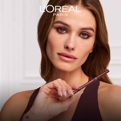 A model with elegant burgundy eye makeup holding the Haute Couleur Kohl Eyeliner near her face to demonstrate its smooth, professional finish.