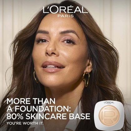 Close-up of a smiling woman (Eva Longoria) with glowing, hydrated skin next to a L'Oréal Paris Hyaluron Tinted Balm compact, featuring the text "MORE THAN A FOUNDATION: 80% SKINCARE BASE".