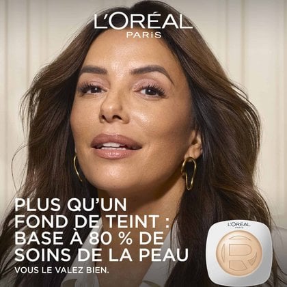 Gros plan d'une femme souriante (Eva Longoria) à la peau éclatante et hydratée à côté d'un poudrier Hyaluron Tinted Balm de L'Oréal Paris, avec le texte "MORE THAN A FOUNDATION: 80% SKINCARE BASE".