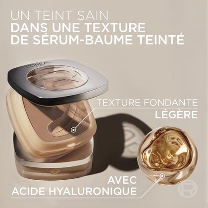 Gros plan du fond de teint baume teinté rond et crémeux dans son boîtier, accompagné de gouttelettes d'hydratation et d'un texte mettant en avant "HEALTHY COMPLEXION IN A TINTED SERUM BALM TEXTURE" et "WITH HYALURONIC ACID".