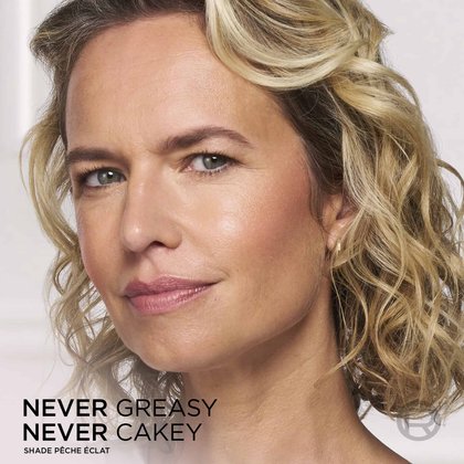 Close-up portrait of a woman showcasing a smooth, flawless, and radiant makeup finish, with the overlay text "NEVER GREASY NEVER CAKEY".