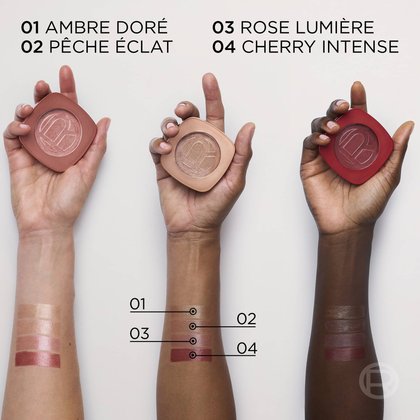 Trois mains tenant les boîtiers à côté de quatre échantillons de couleur appliqués sur un avant-bras, affichant les noms des teintes : "01 AMBER DORÉE", "02 PÊCHE ÉCLAT", "03 ROSE LUMIÈRE" et "04 CHERRY INTENSE".