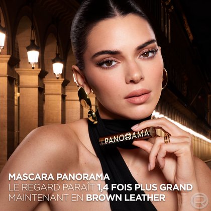 La mannequin Kendall Jenner, maquillée avec le mascara Panorama, tient le tube du produit devant elle. Le texte annonce : "MASCARA PANORAMA LE REGARD PARAÎT 1,4 FOIS PLUS GRAND MAINTENANT EN BROWN LEATHER". Elle est vêtue d'un haut noir et porte de grandes boucles d'oreilles dorées, dans un cadre urbain éclairé.