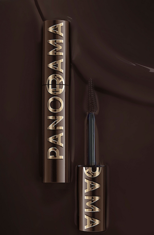A dark bronze mascara tube with "PANORAMA" in slightly raised gold lettering stands vertically on a rich chocolate brown background. The mascara cap is unscrewed and positioned below it, with the dark mascara brush visible, extending upwards. The background features subtle ripples, suggesting a liquid or velvety texture.