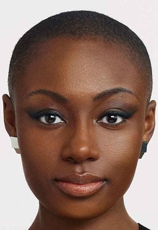 A split image showing the face of a woman with dark skin. The left side displays her natural skin with some minor imperfections, while the right side shows her skin with makeup applied, appearing smoother and more even-toned.