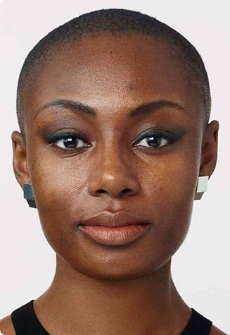 A split image showing the face of a woman with dark skin. The left side displays her natural skin with some minor imperfections, while the right side shows her skin with makeup applied, appearing smoother and more even-toned.