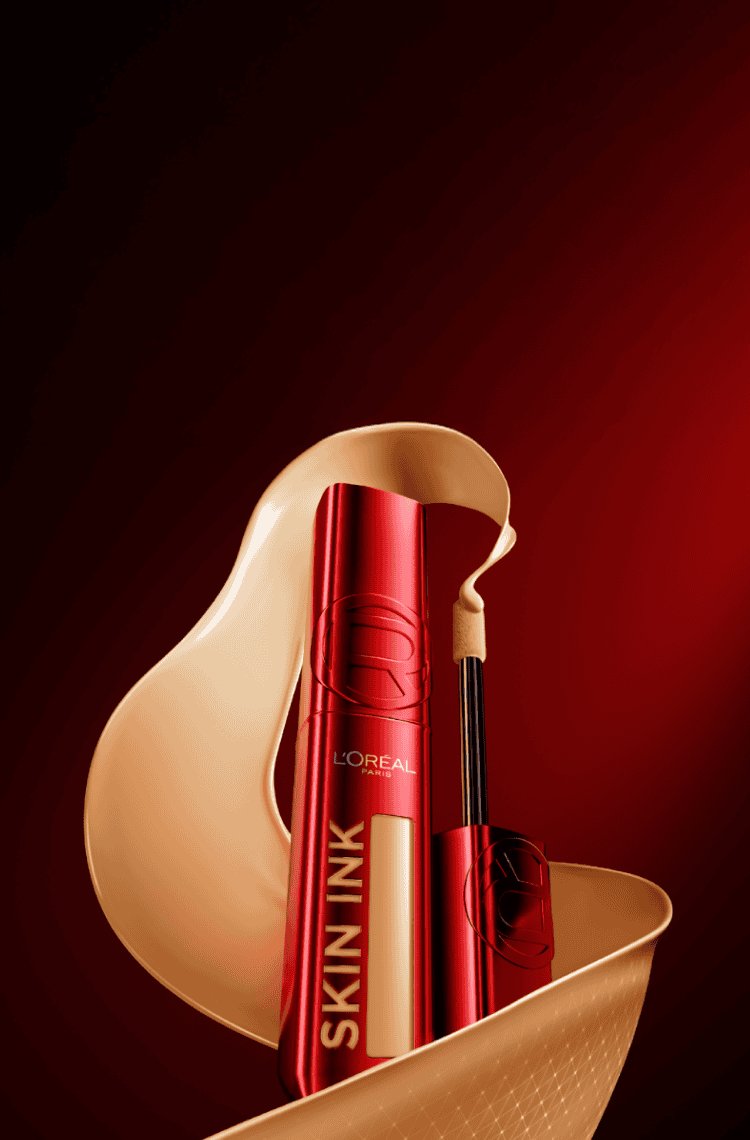 A red L'Oréal Skin Ink product bottle with a clear window displaying the shade is positioned within a swirl of beige liquid foundation, set against a black and red gradient background.