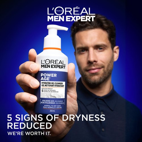 A man with short dark hair and a beard holds the Power Age Hydrating Gel Cleanser bottle close to the camera. The background is a vibrant gradient blue. Large text at the bottom reads "5 SIGNS OF DRYNESS REDUCED" with the L'Oréal slogan "WE’RE WORTH IT."