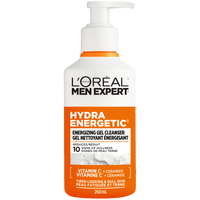 A studio shot of the L'Oréal Paris Men Expert Hydra Energetic Energizing Gel Cleanser bottle (260ml). The white bottle features a bold orange label and a pump dispenser. It is centered against a background of white soapy foam. Text highlights "Vitamin C + Ceramide" and "Tired-Looking & Dull Skin."