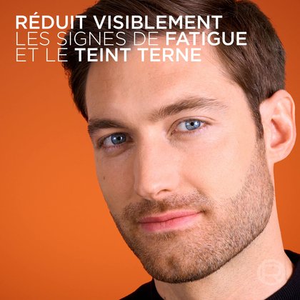 Un gros plan du visage d'un homme à la peau saine sur fond orange. Le texte en haut indique : « RÉDUIT VISIBLEMENT LES SIGNES DE FATIGUE ET LE TEINT TERNE ».