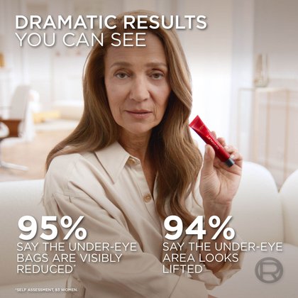 A middle-aged woman with long brown hair, wearing a light-colored shirt, holds up the L'Oréal Revitalift Eye Bag Instant Eraser tube and smiles. Text overlays state: "DRAMATIC RESULTS YOU CAN SEE." Two statistics are displayed: "95% SAY THE UNDER-EYE BAGS ARE VISIBLY REDUCED*" and "94% SAY THE UNDER-EYE AREA LOOKS LIFTED*". An asterisk indicates "SELF ASSESSMENT, 83 WOMEN." The woman is sitting on a white couch in a bright room.