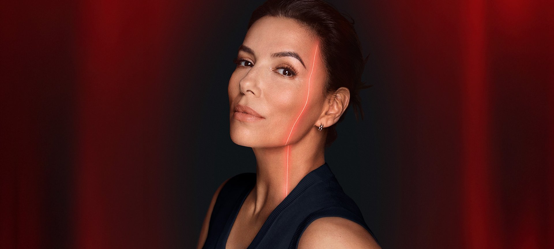 Eva Longoria, égérie de L'Oréal, avec un regard confiant, son visage traversé par une ligne laser rouge, sur un fond sombre dégradé de rouge.