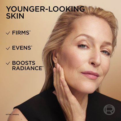 A close-up portrait of actress Gillian Anderson, showcasing her radiant and firm complexion. Overlaying text emphasizes the benefits of "Younger-looking skin," which "Firms*," "Evens*," and "Boosts Radiance*" (after 2 weeks).
