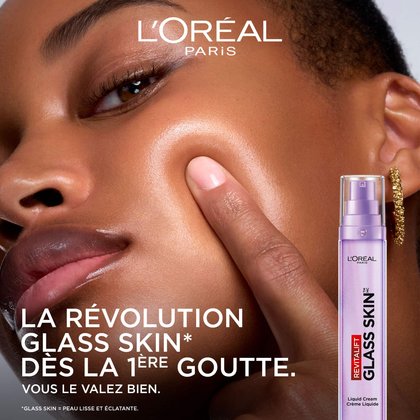 Une femme à la peau éclatante et lisse touche sa joue pour montrer l'effet lumineux du produit. À côté d'elle, le flacon violet est présenté avec le texte : « La révolution Glass Skin dès la 1ère goutte. »